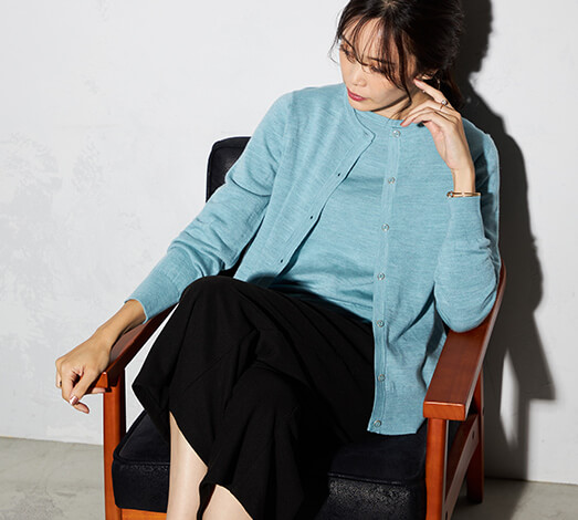 ウールクルーネックニットカーディガンを着用し椅子に座っている女性の写真