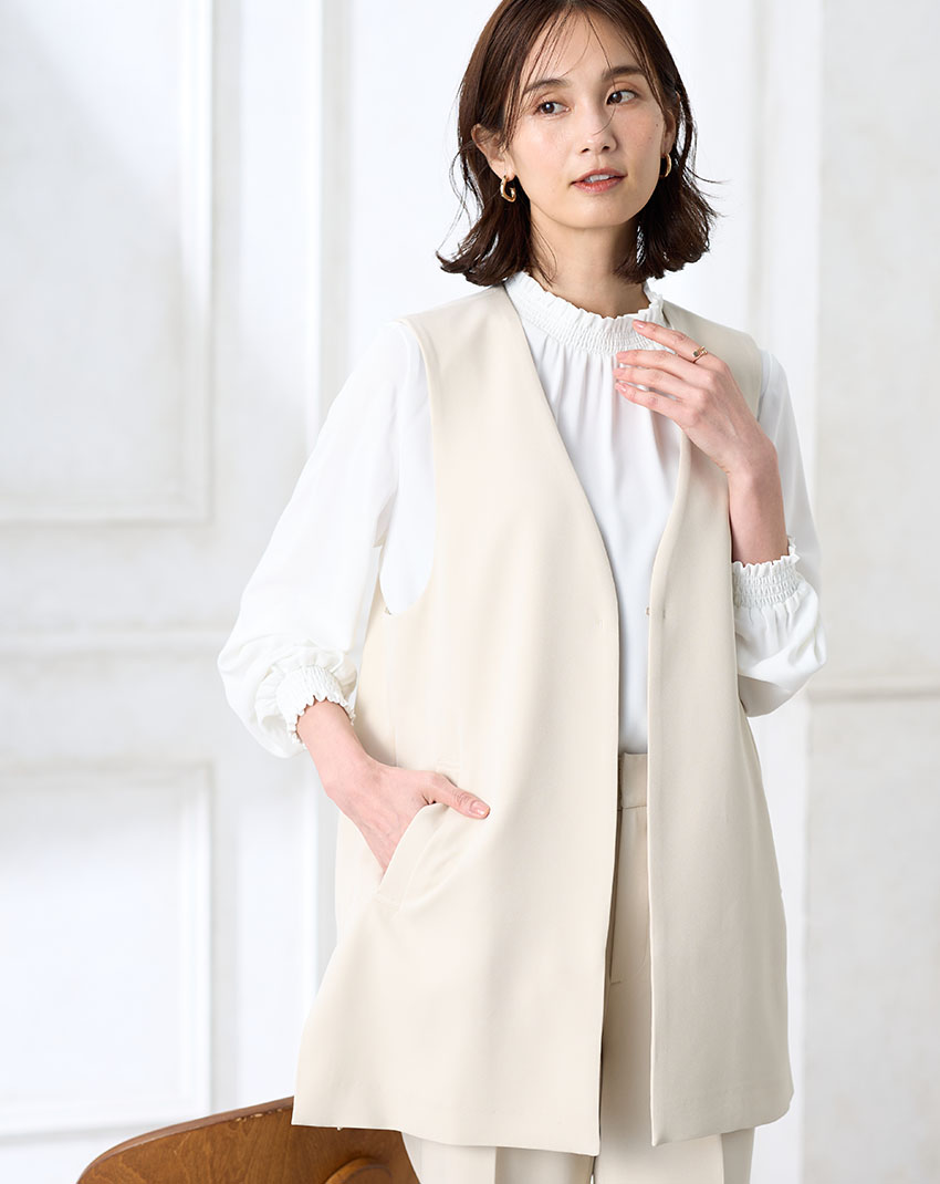 アイボリーのジレジャケット【セットアップ対応】・アイボリーのストレートパンツ【セットアップ対応】・ホワイトのフリルブラウスを着用した女性の画像