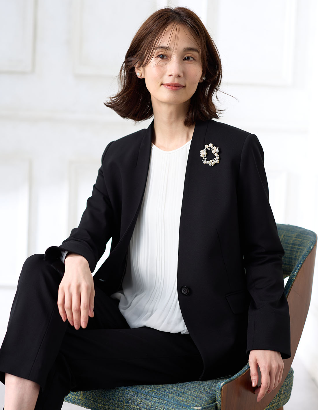 ブラックの【アルファブリック】カラーレスジャケット【セットアップ対応】・ブラックの【アルファブリック】テーパードパンツ【セットアップ対応】・ホワイトのプリーツTブラウスを着用した女性の画像--1