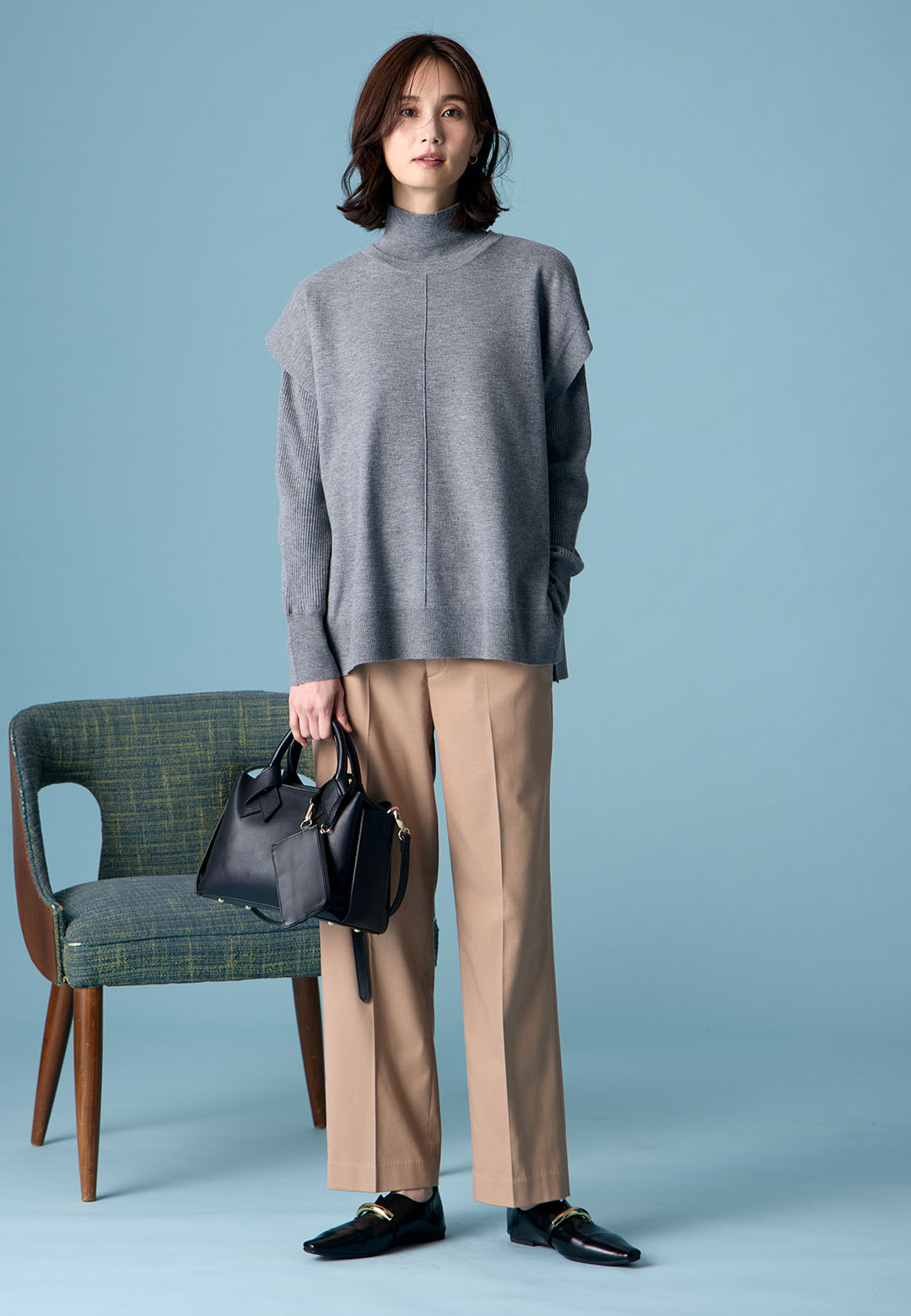 チャコールグレーのハイネックニットアンサンブル・モカの【美モーション】テーパードパンツ・ブラックのバイカラーバッグを着用した女性の画像