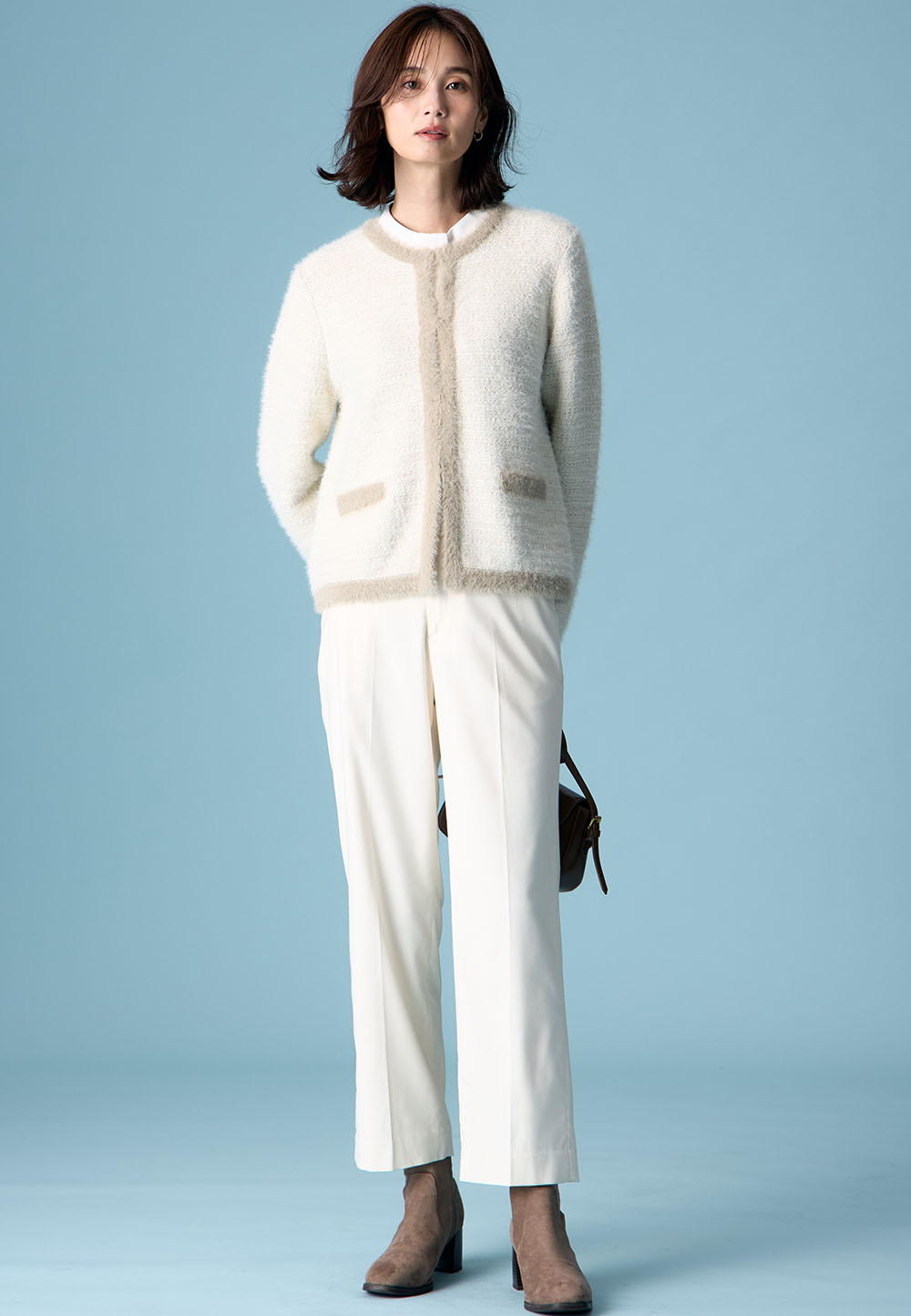 ホワイトのバイカラーニットカーディガン・ホワイトのボウタイブラウス・ホワイトの【美モーション】テーパードパンツ・ブラウンのブーツを着用した女性の画像