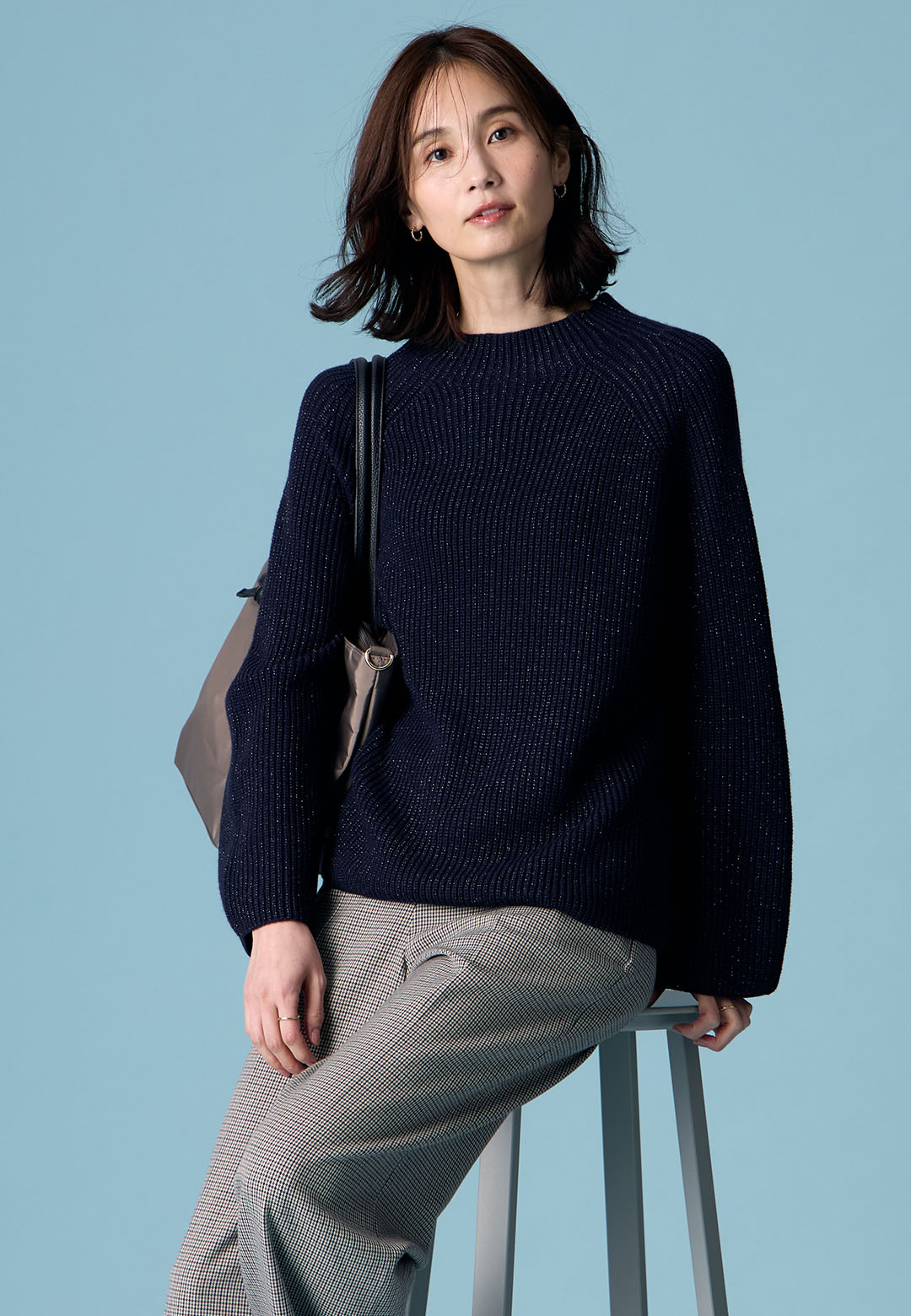 ネイビーのラメニットプルオーバー・ブラックのローズ加工セミワイドパンツ・ブラウンの2WAYトートバッグを着用した女性の画像