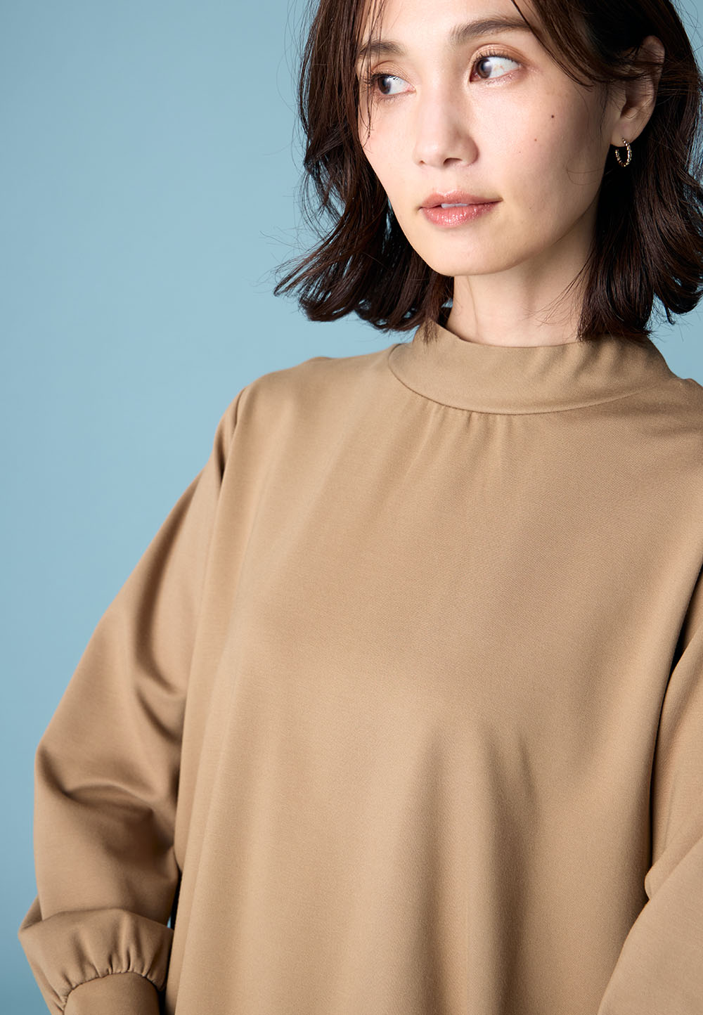 ブラウンのハイネックチュニックを着用した女性のアップの画像