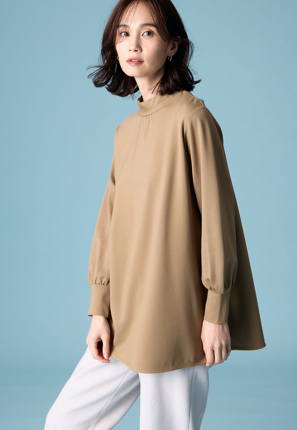 ブラウンのハイネックチュニック・ライトグレーのストレッチ起毛ワイドパンツを着用した女性の画像