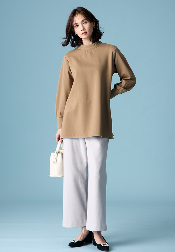 ブラウンのハイネックチュニック・ライトグレーのストレッチ起毛ワイドパンツ・ホワイトのバッグ・ブラックのパンプスを着用した女性の画像