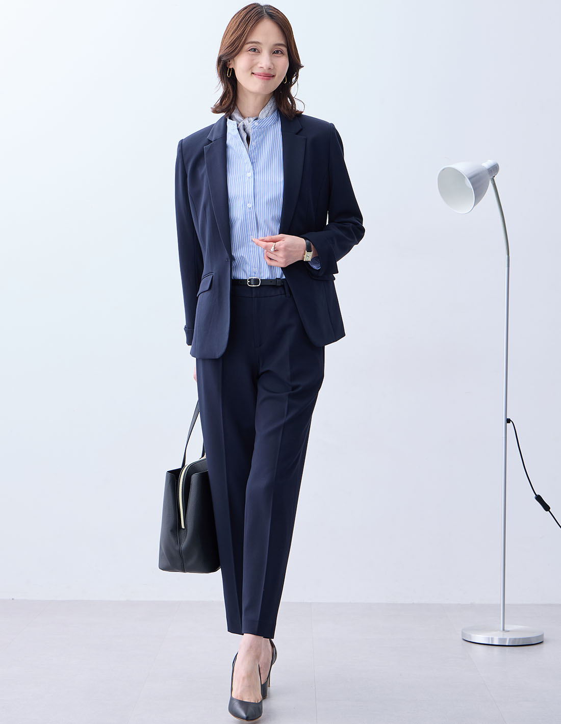 ネイビーの【アルファブリック】テーラードジャケット【セットアップ対応】・サックスブルーのバンドカラーストライプシャツ・ネイビーの【アルファブリック】テーパードパンツ【セットアップ対応】・ブルーのプリントスカーフを着用した女性の画像