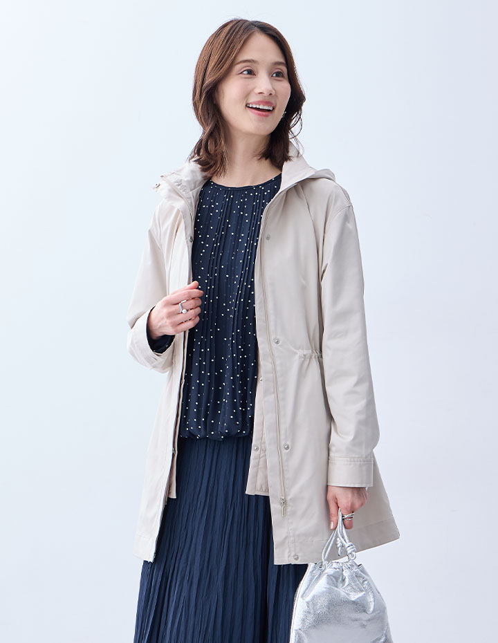 ライトベージュの3WAYコート【スーパーウォーム】【ライナー付き】・ブラックのジャガードTブラウス・ネイビーのプリーツスカートを着用した女性の画像