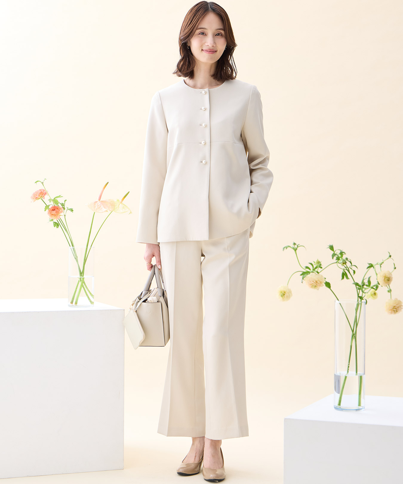 ベージュのペプラムジャケット・ベージュのストレートパンツ・ベージュのバイカラーバッグを着用した女性の画像