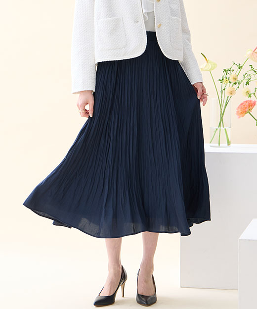 オフホワイトのツイードジャケット・ホワイトのジャガードボウタイブラウス・ネイビーのプリーツスカート・パールモチーフブローチを着用した女性の足元の画像（ポイント）