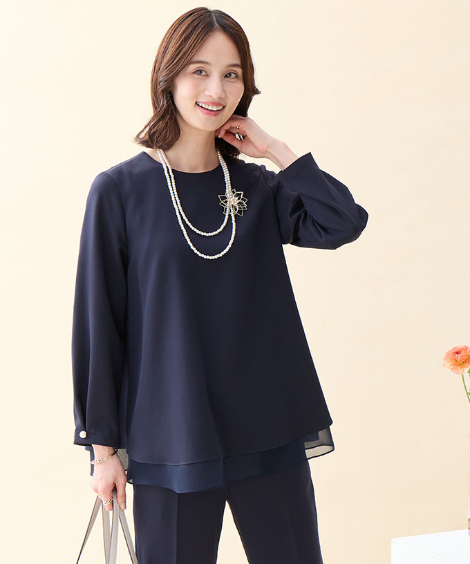 ネイビーのシフォンレイヤードブラウス・ネイビーのストレートパンツ・ブローチ付きネックレス・ベージュのトートバッグを着用した女性の画像--1