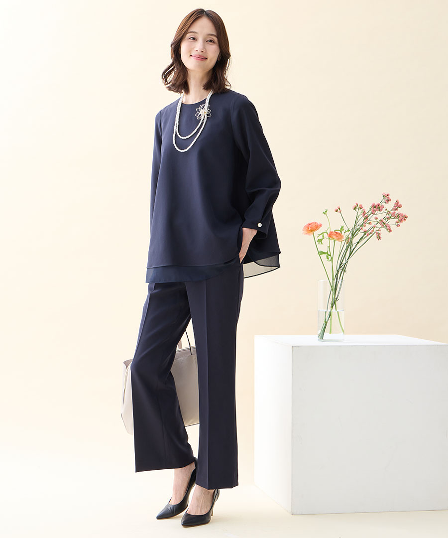 ネイビーのシフォンレイヤードブラウス・ネイビーのストレートパンツ・ブローチ付きネックレス・ベージュのトートバッグを着用した女性の画像--2