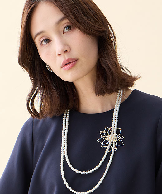 ネイビーのシフォンレイヤードブラウス・ネイビーのストレートパンツ・ブローチ付きネックレスを着用した女性の画像（ポイント）