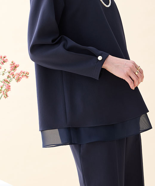 ネイビーのシフォンレイヤードブラウス・ネイビーのストレートパンツ・ブローチ付きネックレスを着用した女性の手元の画像（ポイント）