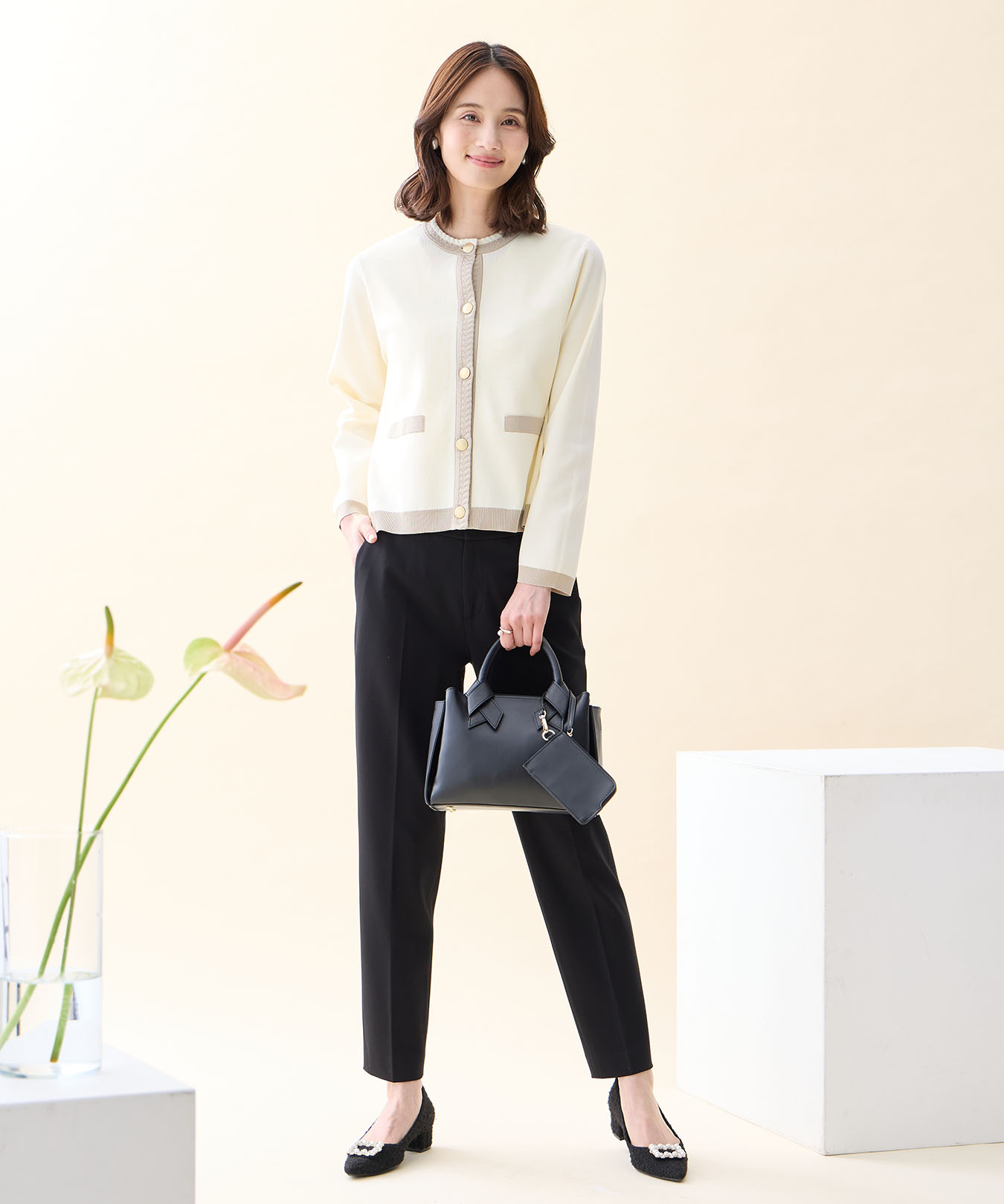オフホワイトのバイカラーニットカーディガン・ブラックの【アルファブリック】テーパードパンツ・ブラックのバイカラーバッグを着用した女性の画像