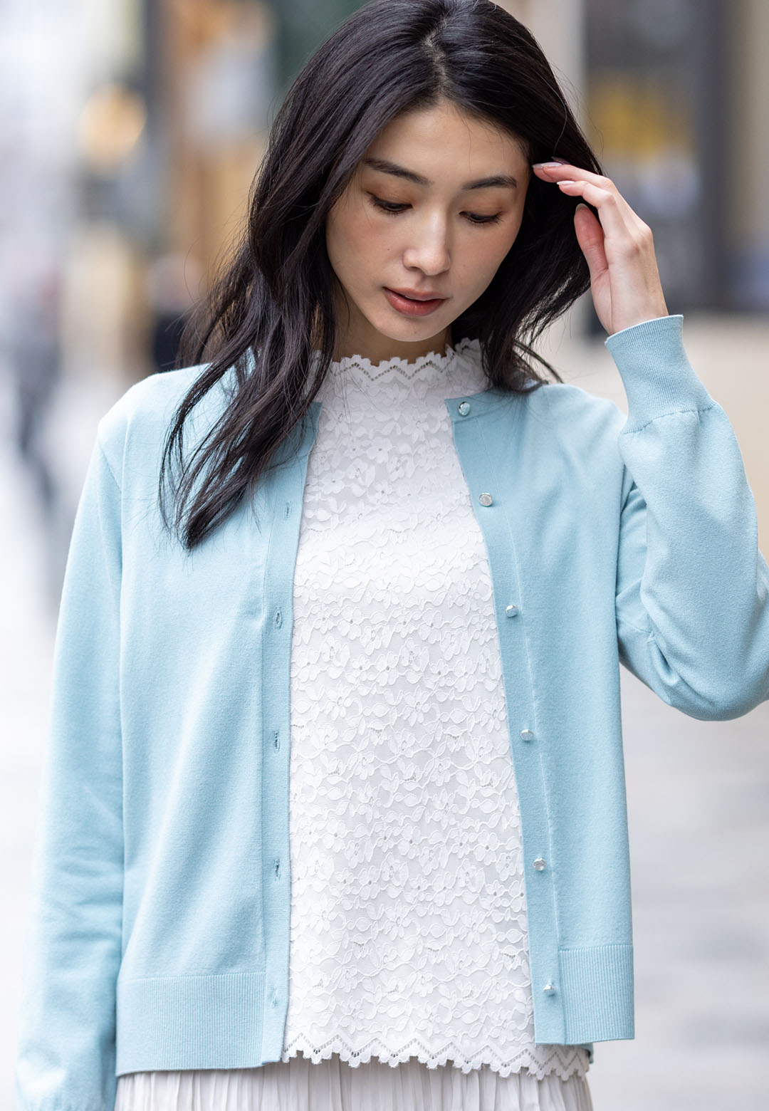 オフホワイトのフロントレースハイネックプルオーバー・ミントグリーンのクルーネックニットカーディガン・ベージュのプリーツスカートを着用した女性の画像--2