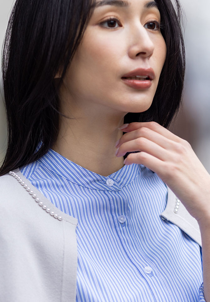ライトグレーのパールボタンニットカーディガン・ブルーのバンドカラーストライプシャツを着用した女性のアップの画像