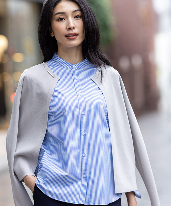 ライトグレーのパールボタンニットカーディガン・ブルーのバンドカラーストライプシャツ・ネイビーのストレッチ テーパードパンツを着用した女性の画像（アンカーリンク）