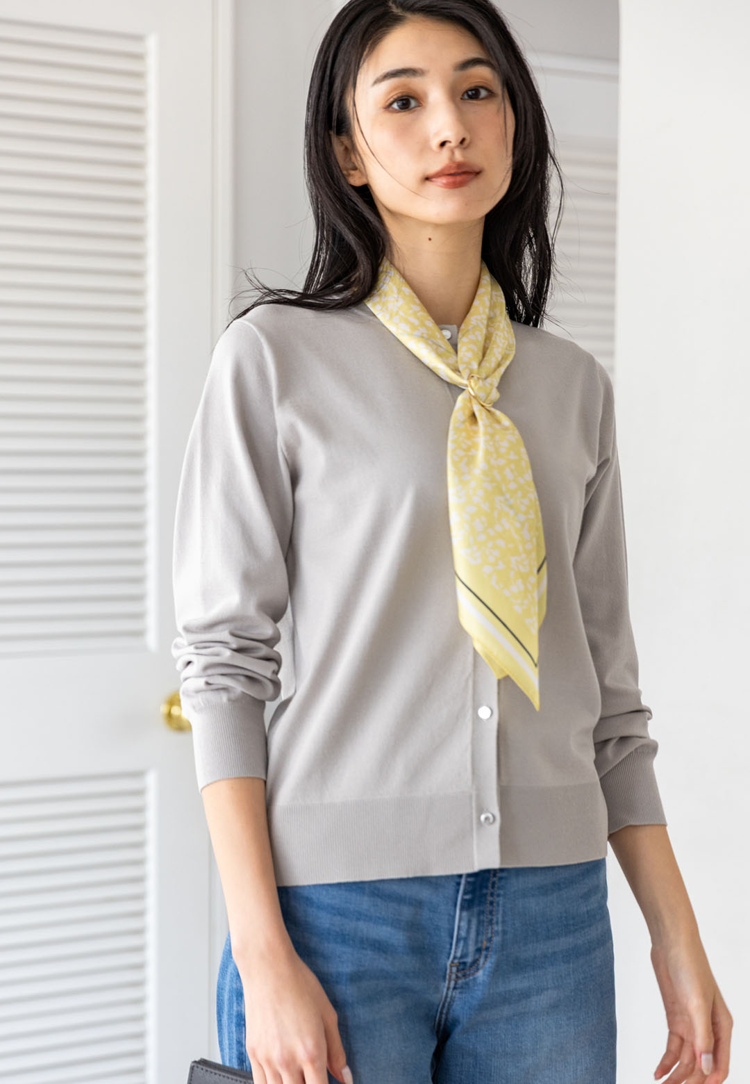 ライトグレーのクルーネックニットカーディガン・ブルーのデニムパンツ・イエローのリング付きスカーフを着用した女性の画像--1