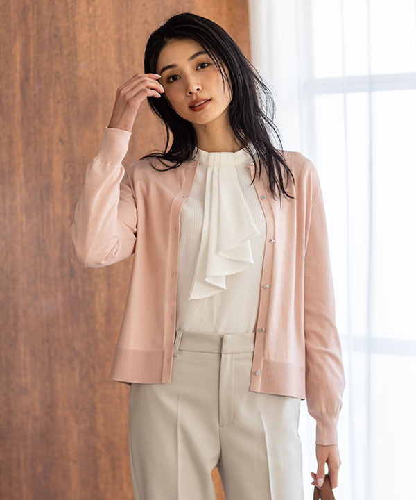 ピンクのクルーネックニットカーディガン・オフホワイトのジャガードボウタイブラウス・アイボリーのストレッチ テーパードパンツを着用した女性の画像（アンカーリンク）