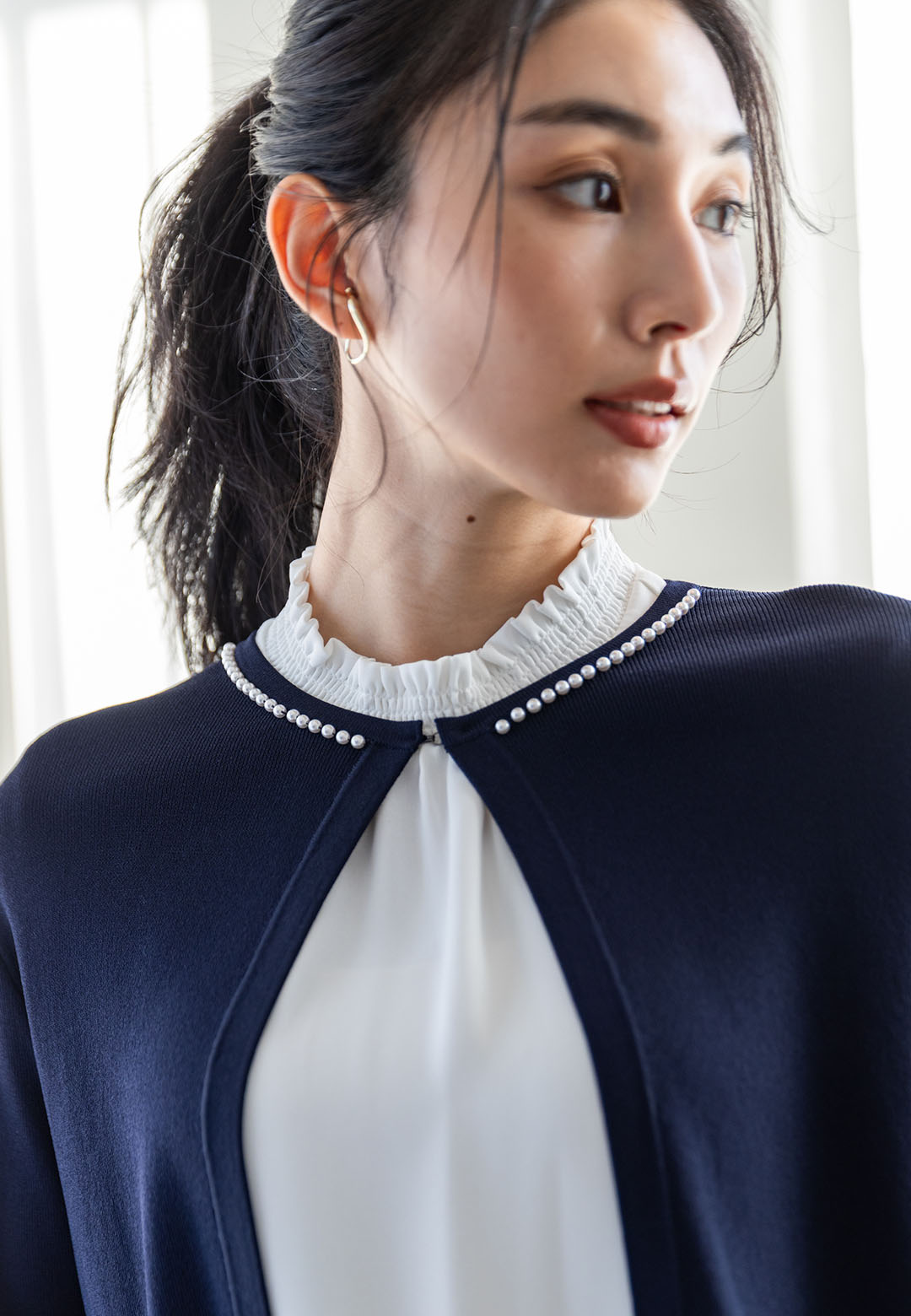ネイビーのパールボタンニットカーディガン・オフホワイトのフリルブラウスを着用した女性のアップの画像
