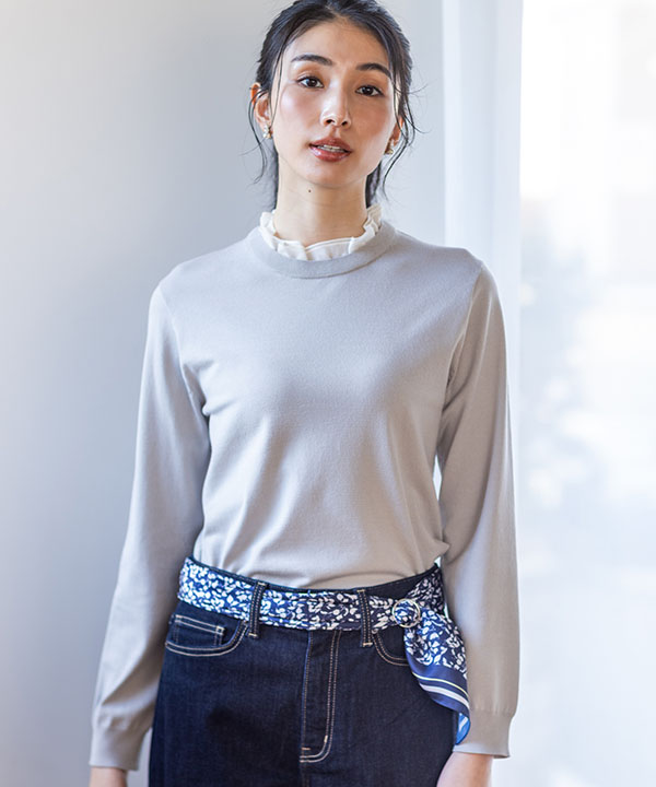 グレージュのフリルカラードッキングプルオーバー・ネイビーのデニムパンツ・ブルーのリング付きスカーフを着用した女性の画像（アンカーリンク）