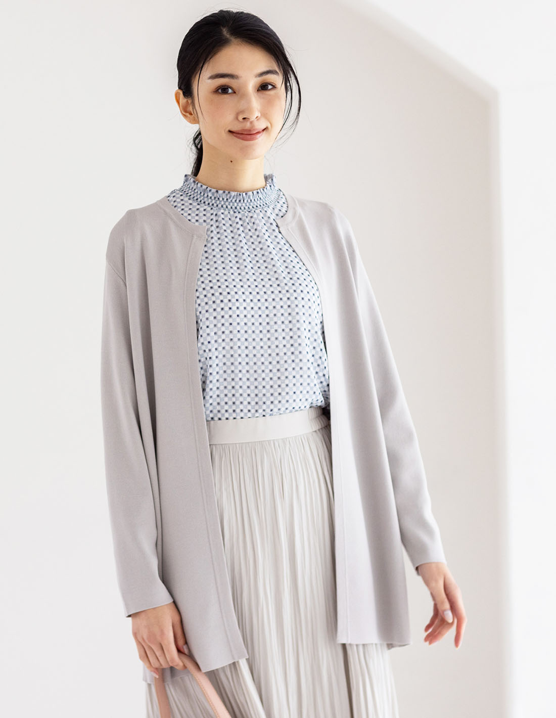 ライトグレーのクルーネックニットロングカーディガン・サックスのジャガードTブラウス・ベージュのプリーツスカートを着用した女性の画像--1