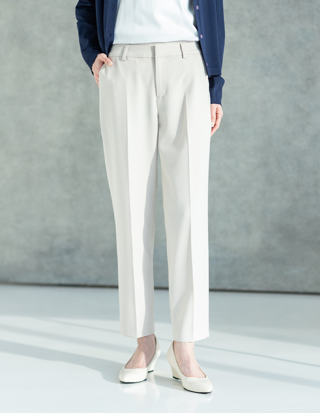 ライトベージュのストレッチテーパードパンツ・ネイビーのクルーネックカーディガン・オフホワイトのレースドッキングプルオーバーを着用した女性の足元の画像