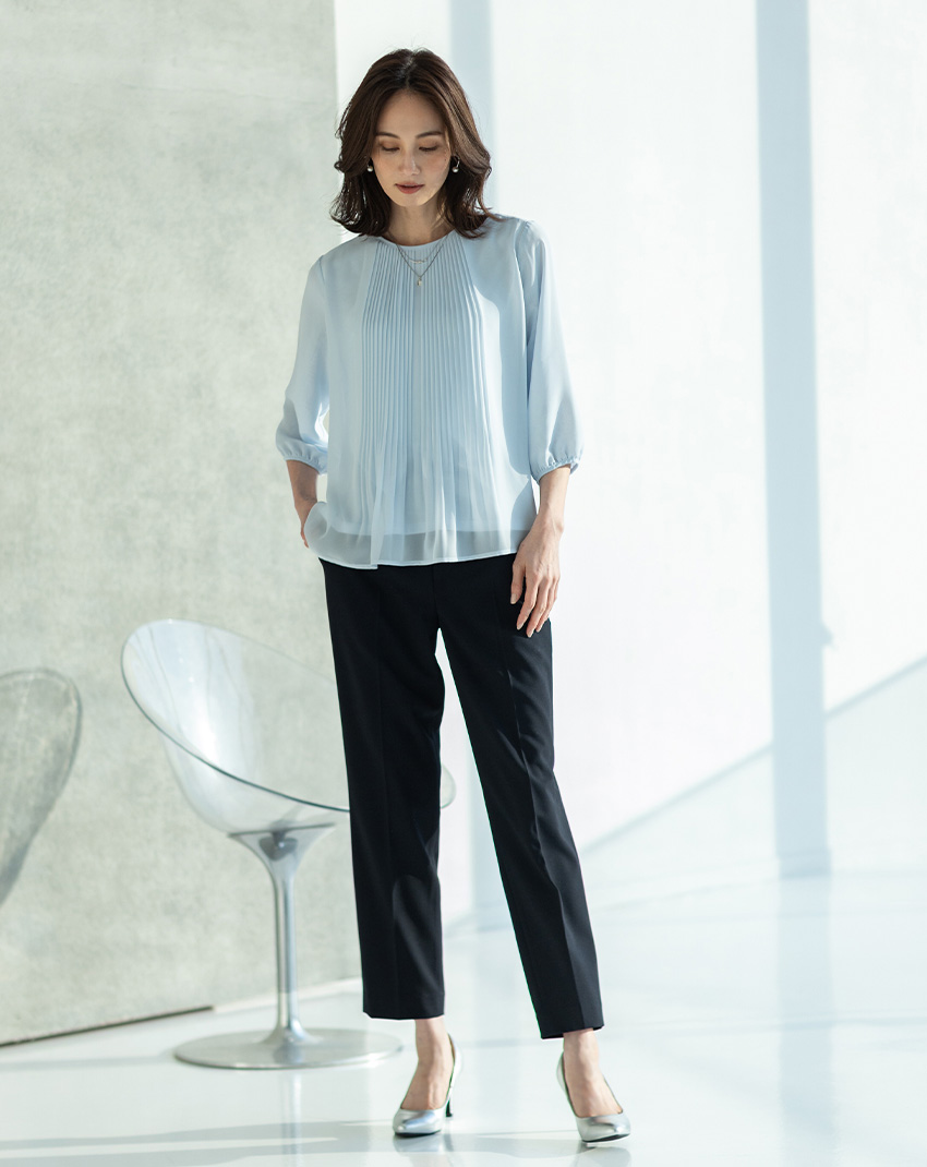ブルーのシフォンプリーツＴブラウス・ネイビーのストレッチテーパードパンツ・２連モチーフトップネックレスを着用した女性の画像