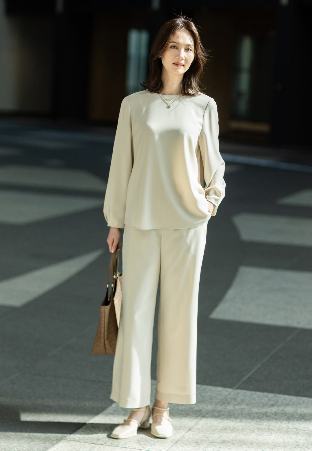 ストレッチジョーゼットタックブラウス【セットアップ対応】、ストレッチジョーゼットストレートパンツ【セットアップ対応】、編み込み風合皮トートバッグを着用した女性の画像--1
