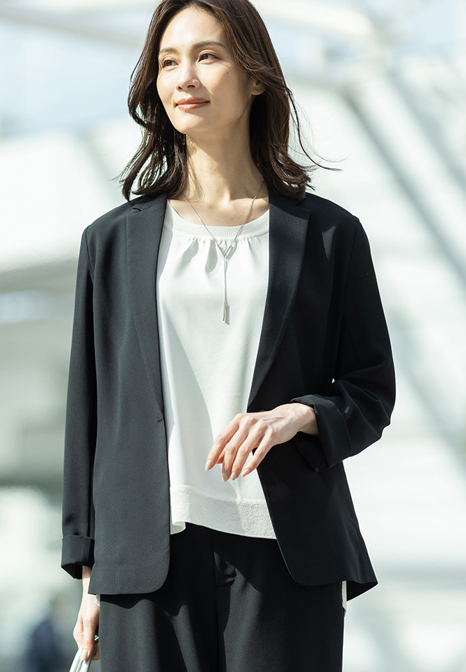 ストレッチジョーゼットテーラードジャケット【セットアップ対応】、ストレッチジョーゼットストレートパンツ【セットアップ対応】、Ｖモチーフネックレスを着用した女性のアップの画像