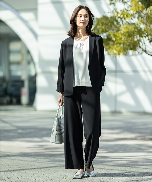 ストレッチジョーゼットカラーレスジャケット【セットアップ対応】、ストレッチジョーゼットストレートパンツ【セットアップ対応】、Ｖモチーフネックレスを着用した女性の画像（アンカーリンク）