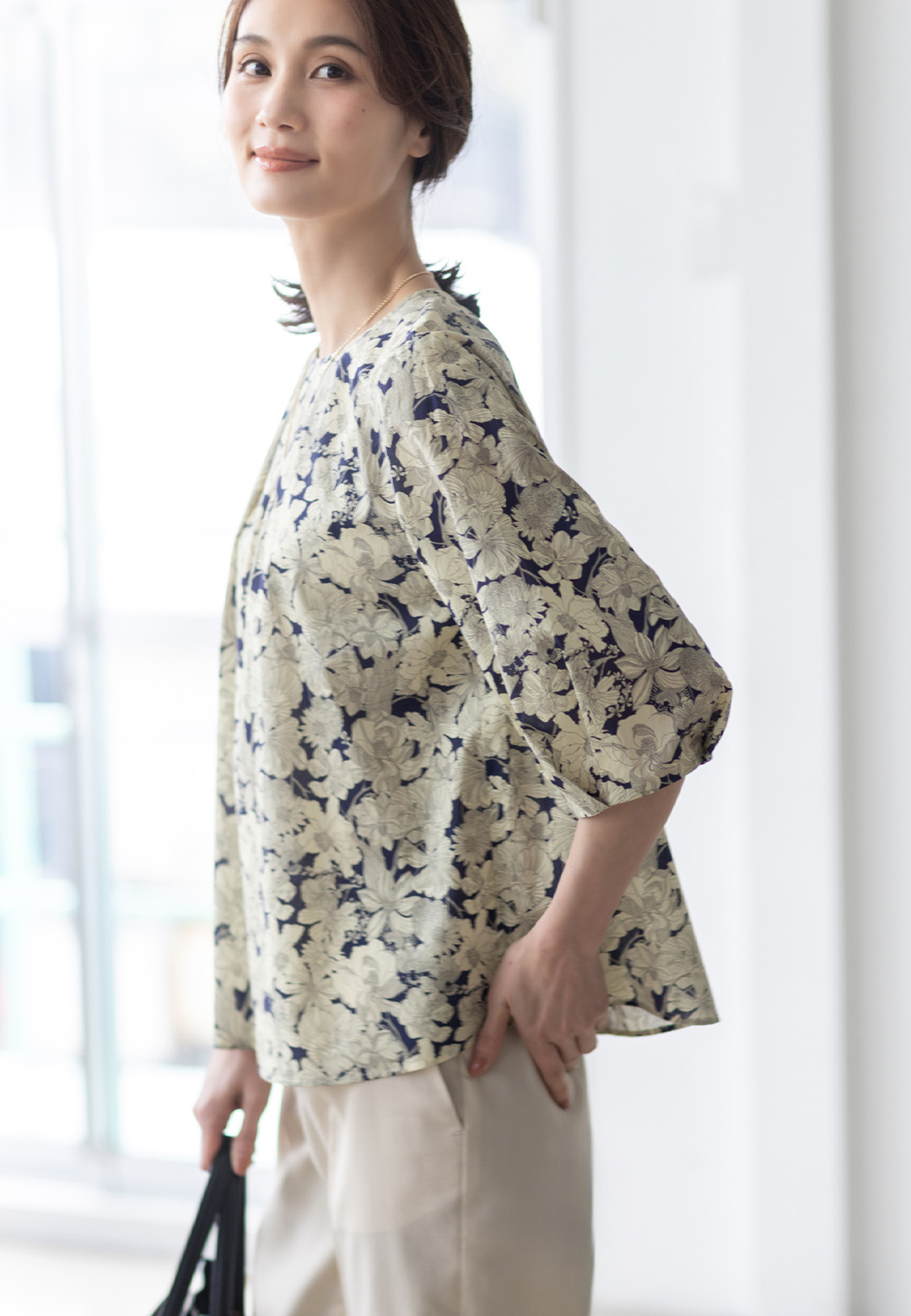 リバティプリントタックスリーブブラウス、バーズアイストレッチクロップドパンツ、ボールチェーンネックレスを着用した女性の画像