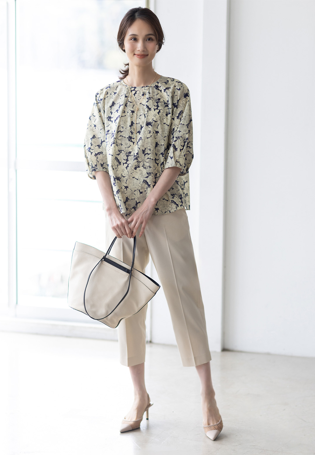 リバティプリントタックスリーブブラウス、バーズアイストレッチクロップドパンツ、ボールチェーンネックレスを着用した女性の全身画像