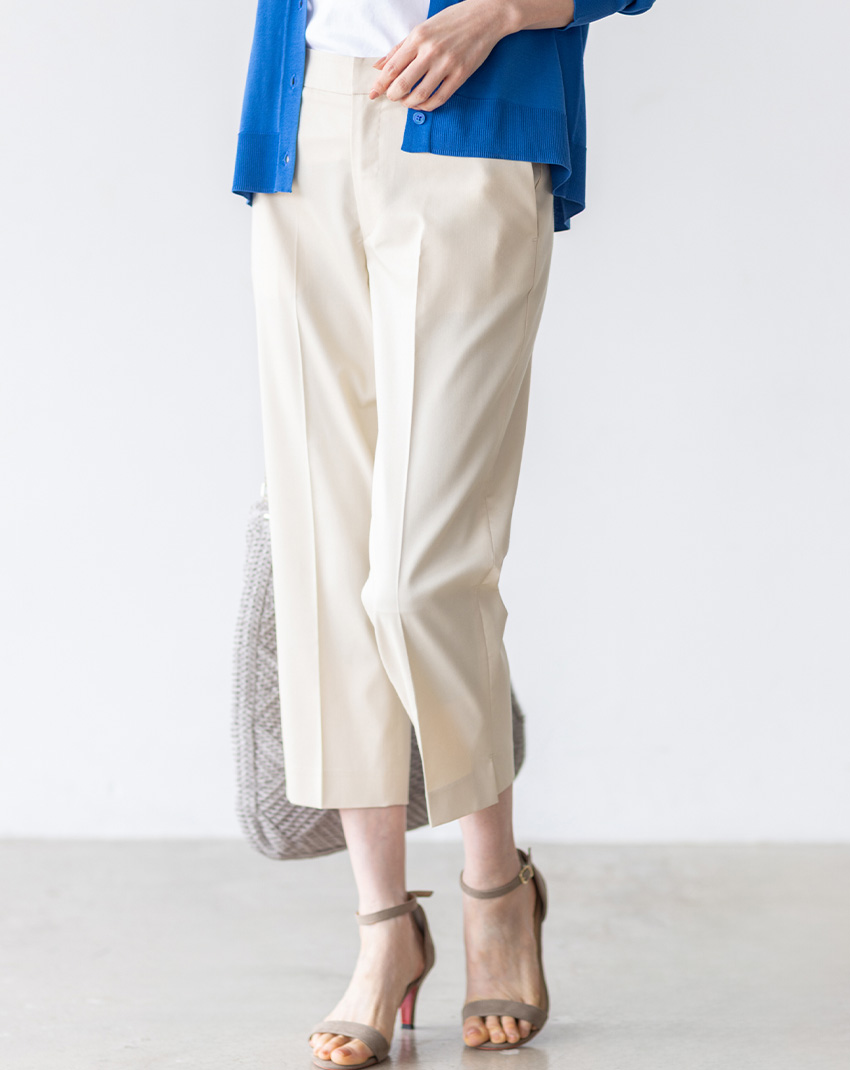 ベージュのバーズアイストレッチクロップドパンツ・ブルーのVネックカーディガン・ホワイトのグラフィックロゴTシャツ・リバティプリントワンショルダーバッグを着用した女性の足元