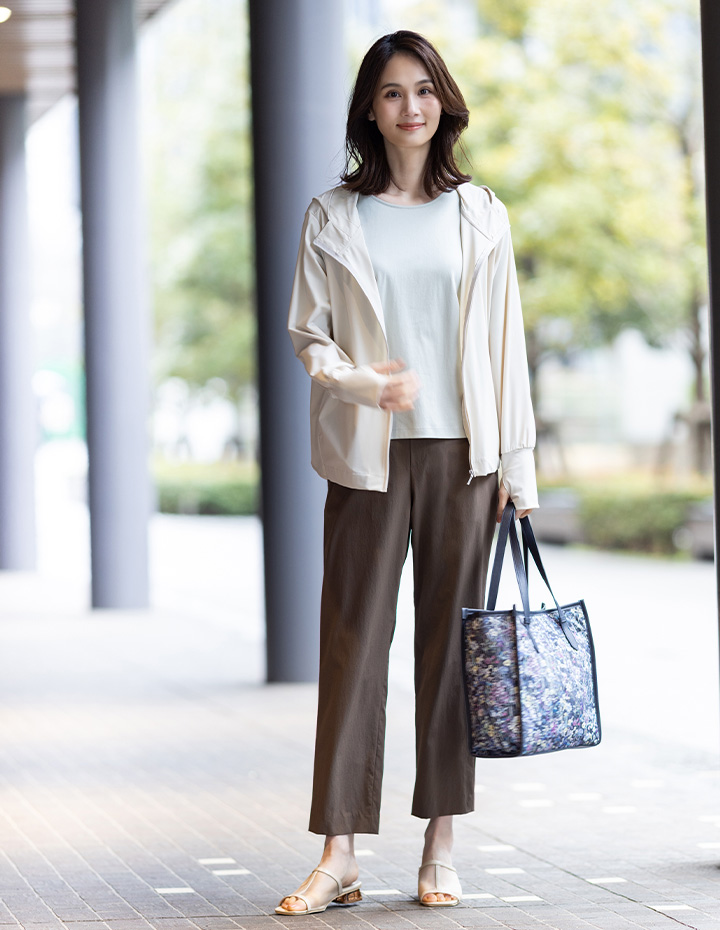 ブラウンのストレッチストレートパンツ・ベージュのラッシュパーカー・ライトグレーのクルーネックTシャツ【すごツヤ・UVカット・接触冷感】・リバティプリントトートバッグを着用した女性