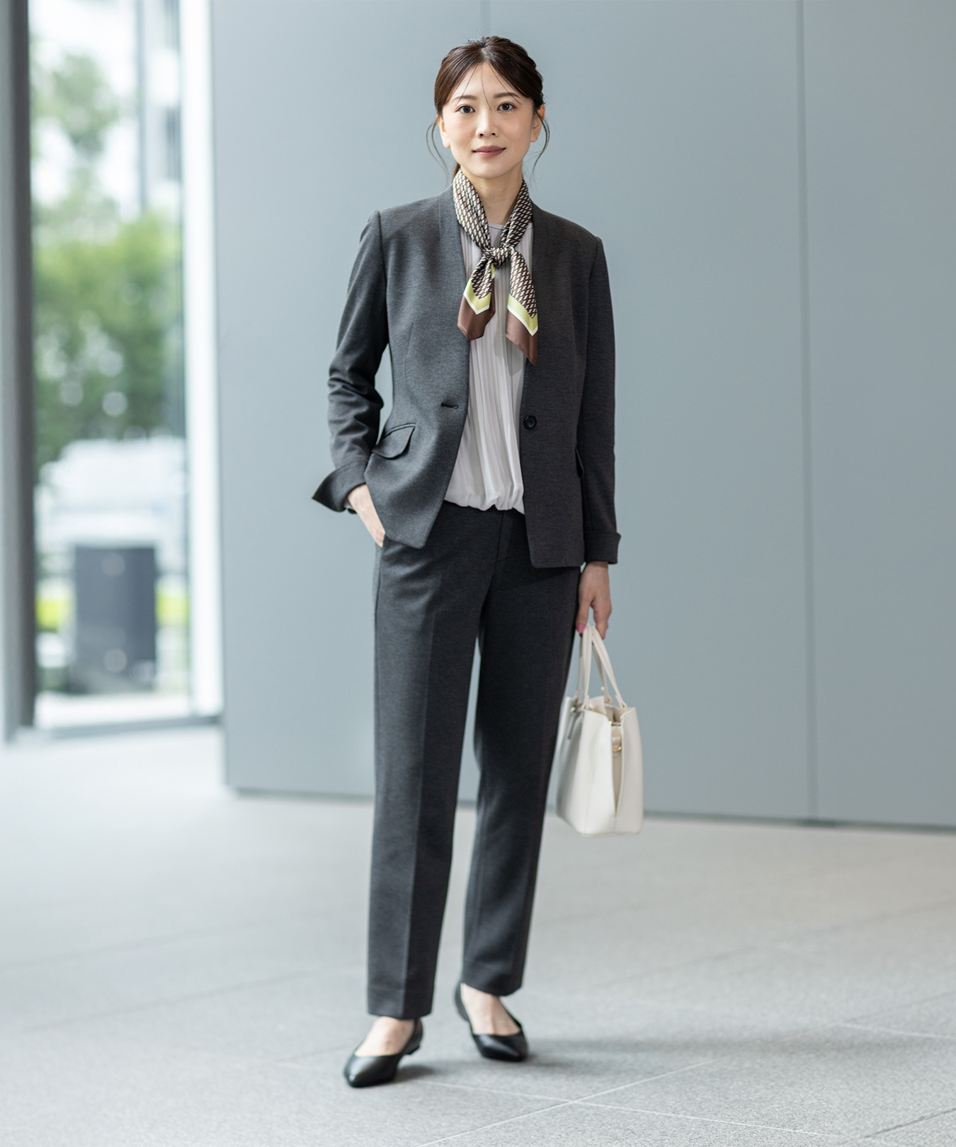 グレーのジャケットとグレーのテーパードパンツを着用し、立っている女性