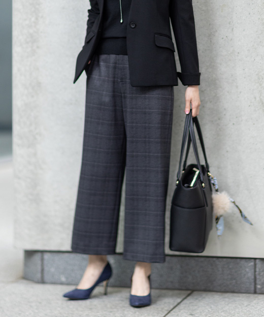 グレーのワイドパンツ・ブラックのトップス・ブラックのジャケットを着用し、立っている女性の足元