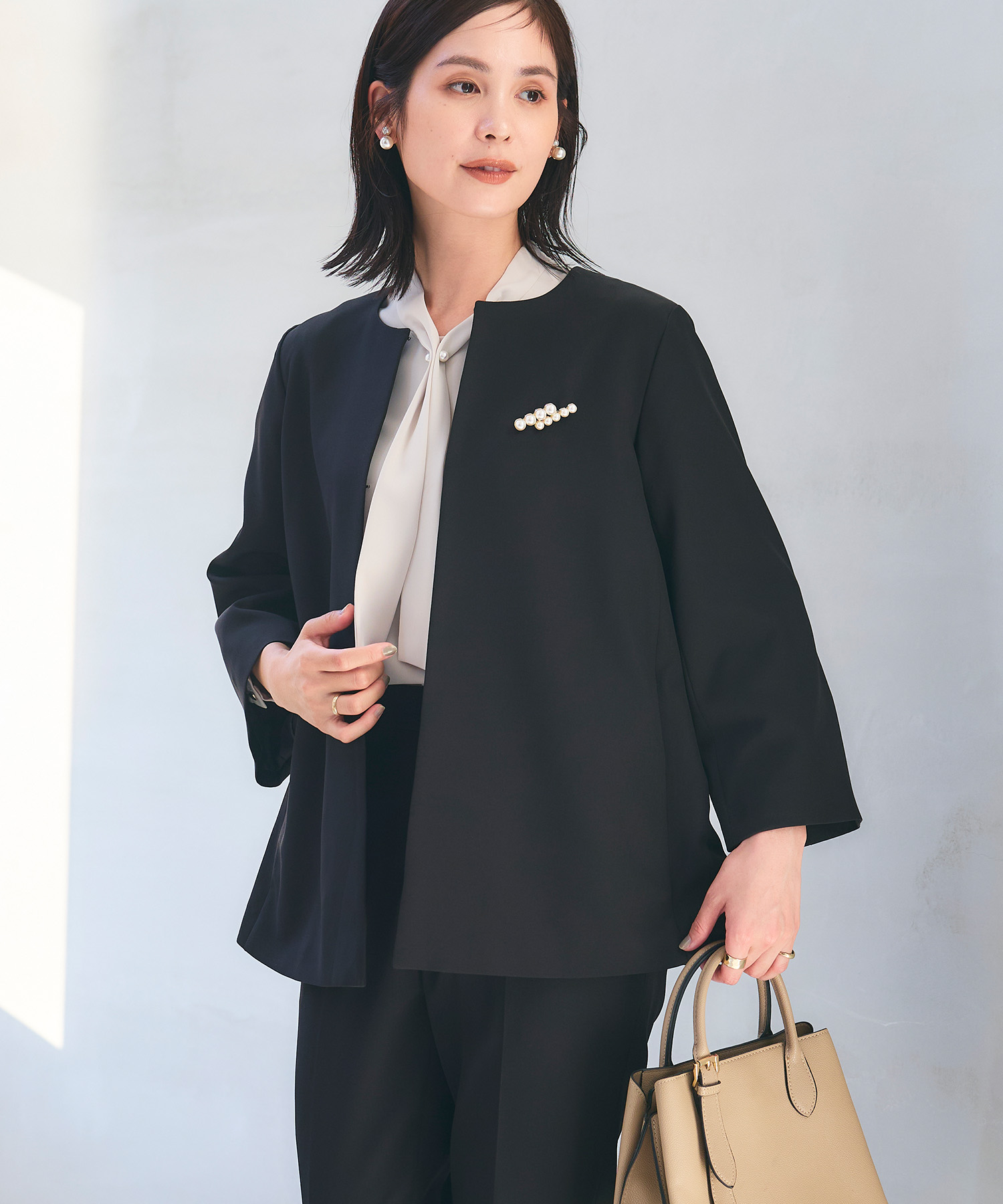 ネイビーの《洗える・シワになりにくい》正解Aラインフレアジャケット・ネイビーの《洗える・シワになりにくい》正解テーパードパンツ・オフホワイトの《シワになりにくい》シルキーサテンパールボウタイブラウスを着用した女性の画像（スライド）