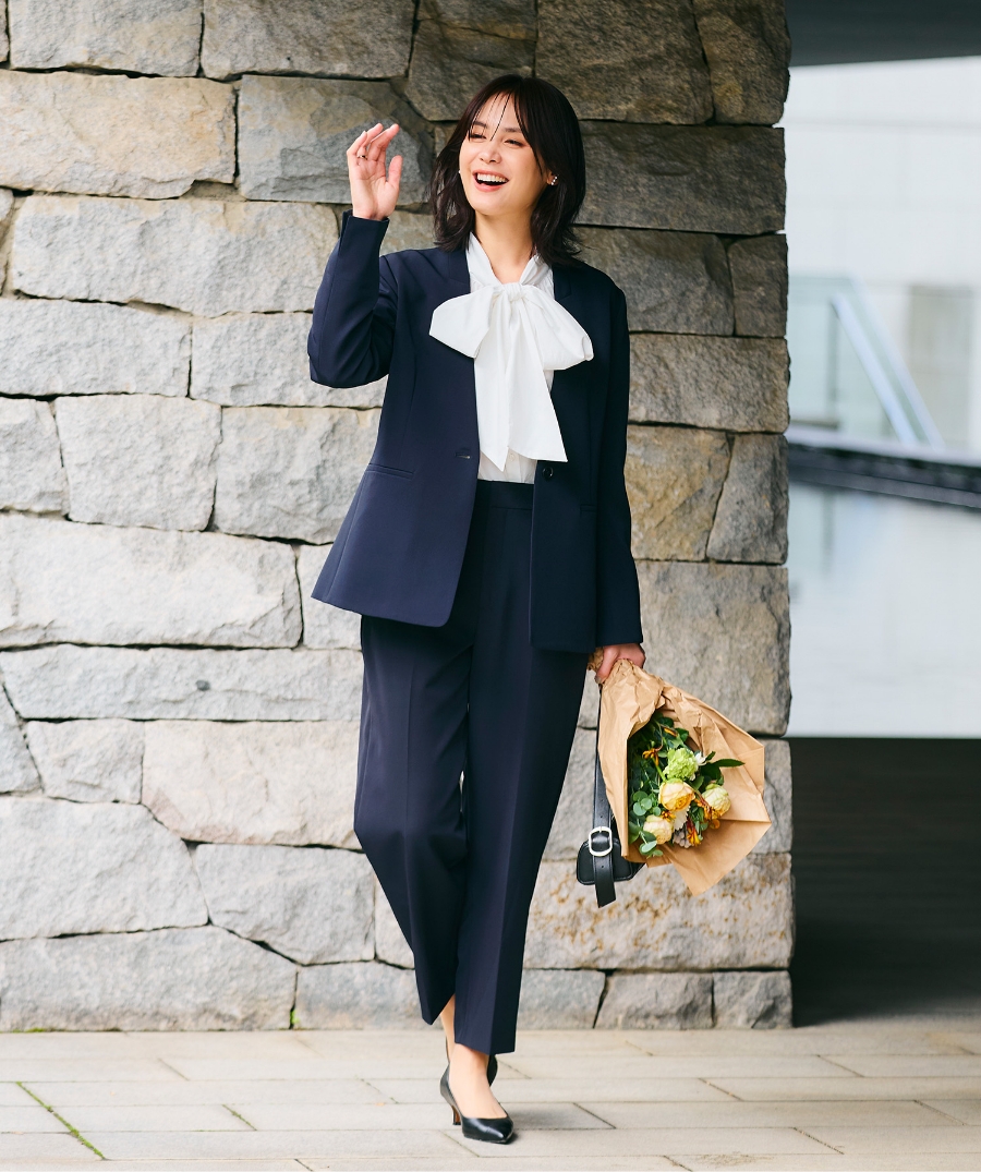 ネイビーの《洗える・シワになりにくい》正解ノーカラージャケット・ネイビーの《洗える・シワになりにくい》正解ワイドパンツ・オフホワイトの《シワになりにくい》リボンボウタイボリュームシャツを着用した女性の画像