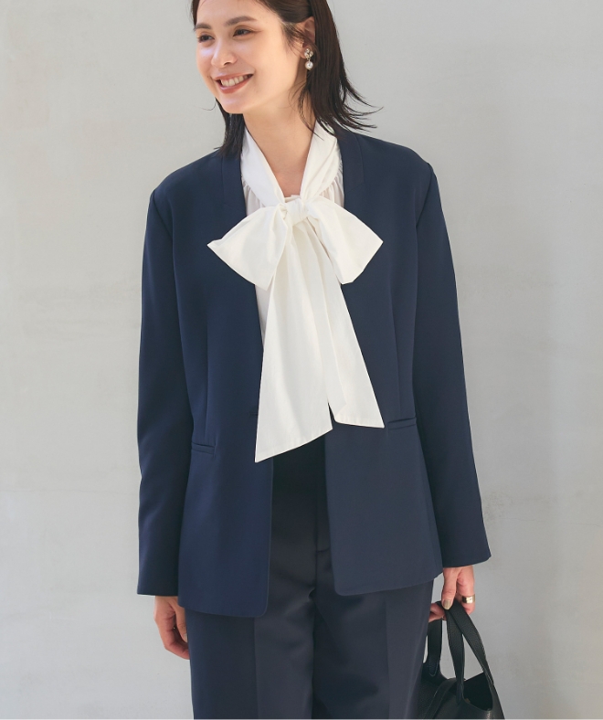 ネイビーの《洗える・シワになりにくい》正解ノーカラージャケット・ネイビーの《洗える・シワになりにくい》正解ワイドパンツ・オフホワイトの《シワになりにくい》リボンボウタイボリュームシャツを着用した女性の画像（スライド）