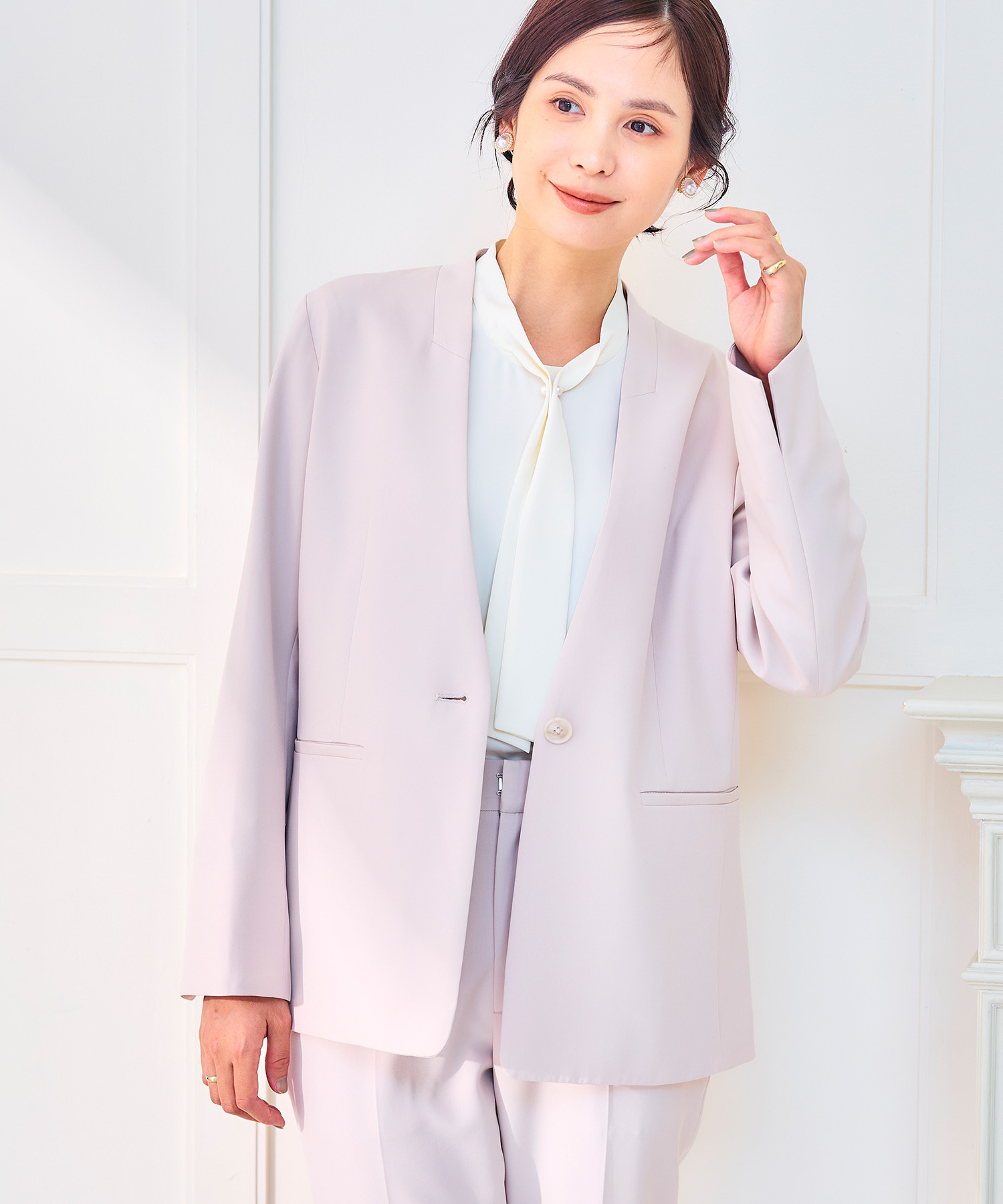 オフベージュの《洗える・シワになりにくい》正解ノーカラージャケット・オフベージュの《洗える・シワになりにくい》正解ワイドパンツ・オフホワイトの《シワになりにくい》シルキーサテンパールボウタイブラウスを着用した女性の画像（スライド）