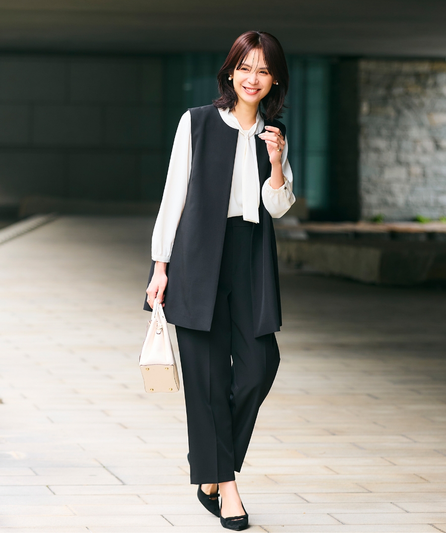 ブラックの《洗える・シワになりにくい》正解ロングジレ・ブラックの《洗える・シワになりにくい》正解ワイドパンツ・オフホワイトの《シワになりにくい》シルキーサテンパールボウタイブラウスを着用した女性の画像