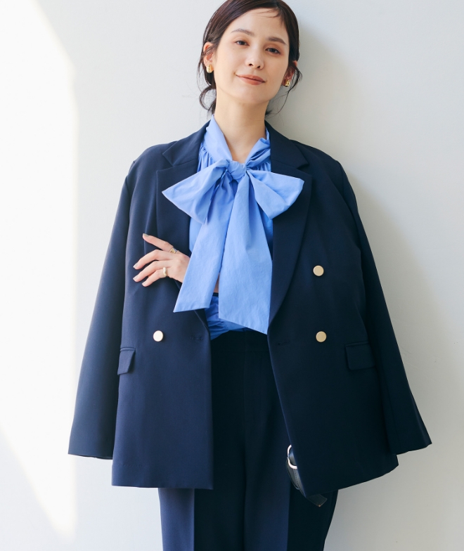 ネイビーの《洗える・シワになりにくい》正解 金釦ダブルテーラードジャケット・ネイビーの《洗える・シワになりにくい》正解 センタープレスストレートパンツ・ブルーの《シワになりにくい》リボンボウタイボリュームシャツを着用した女性の画像（サムネイル）