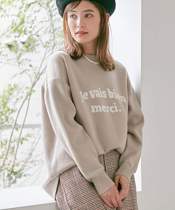 ロゴニットプルオーバーのベージュを着用している女性の写真