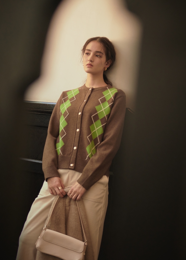 ブラウンのアーガイルカーディガン・アイボリーのコーデュロイスカートを着用した女性の画像