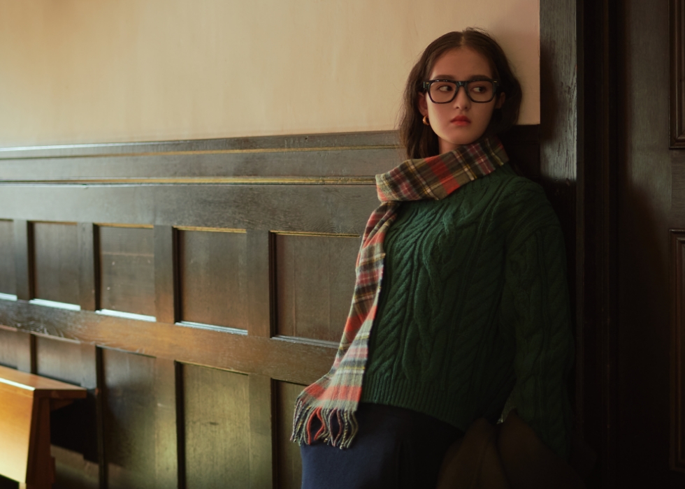 グレージュの丸衿ウールジャケット・ダークグリーンのケーブル編みハイネックニット・ネイビーのウールメルトン台形スカート・オレンジのロキャロンカシミアチェック柄マフラーを着用した女性の画像--1