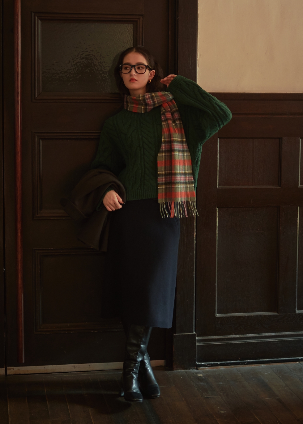 グレージュの丸衿ウールジャケット・ダークグリーンのケーブル編みハイネックニット・ネイビーのウールメルトン台形スカート・オレンジのロキャロンカシミアチェック柄マフラーを着用した女性の画像--3