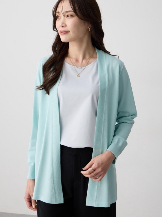 グリーンの着流しロングカーディガン・ホワイトのトップス・ブラックのパンツを着用した女性