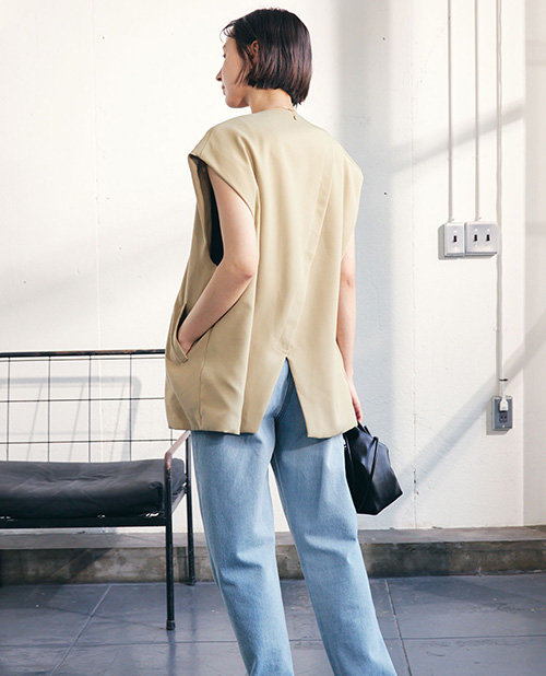 【TOMOコラボ】ノーカラージレベストのベージュを着用して後ろを向いている女性の写真