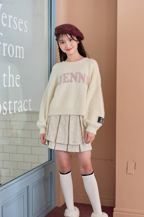 アイボリーのJENNIロゴシャギーニットとプリーツスカートを着た女の子
